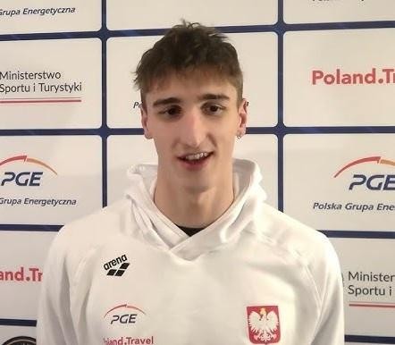 Pływak trenujący intensywnie w nowoczesnym ośrodku pływackim w Teksasie, pod okiem trenera obserwującego z brzegu basenu, symbolizujący zaangażowanie w rozwój sportowy.