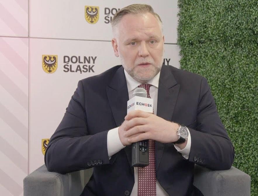 Dawid Jackiewicz podczas wystąpienia publicznego, z gestykulacją, w dynamicznej pozie, symbolizującej jego zaangażowanie w politykę.