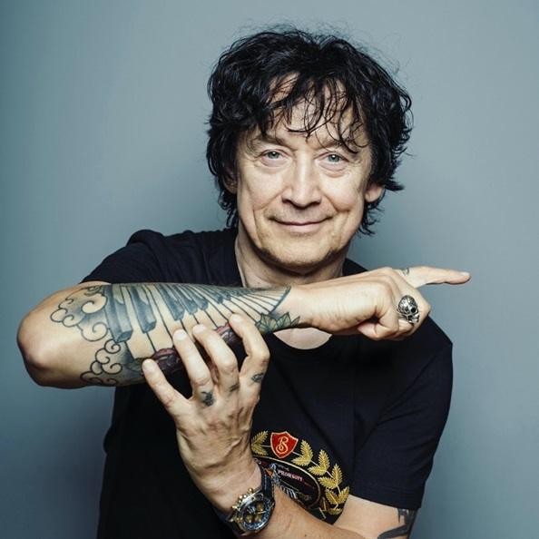 Jan Borysewicz w zbliżeniu, grający na gitarze elektrycznej na scenie, z pasją i skupieniem.