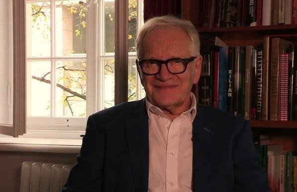 Andrzej Seweryn w zamyślonej pozie w teatralnym otoczeniu, oddający głębię jego artystycznej natury.