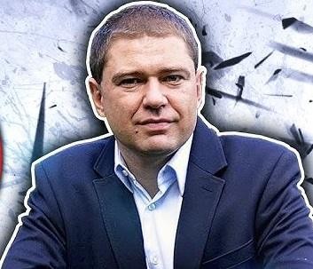Piotr Szumlewicz podczas wystąpienia publicznego, gestykulujący, przemawiający do publiczności, z tłem sugerującym konferencję lub studio telewizyjne.