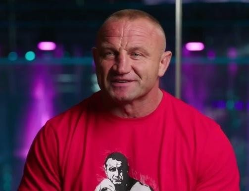 Mariusz Pudzianowski w oktagonie MMA, dynamiczne ujęcie podczas walki, podkreślające jego siłę i determinację.