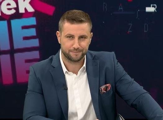 Miłosz Kłeczek podczas burzliwej dyskusji na antenie, gestykulujący z ekspresją, na tle studia telewizyjnego.